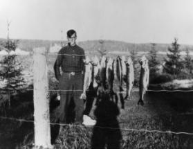 Tom Thomson with fish in front of Mowat Lodge, Algonquin Park